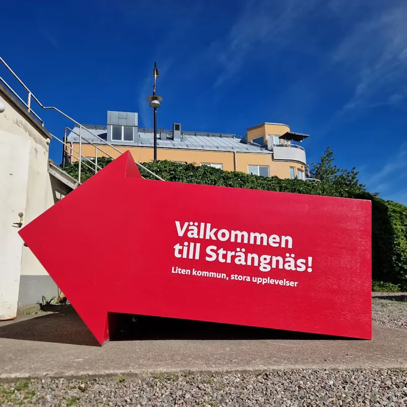 Stor rosa/röd pilformad låda med Välkommen till Strängnäs som textpå